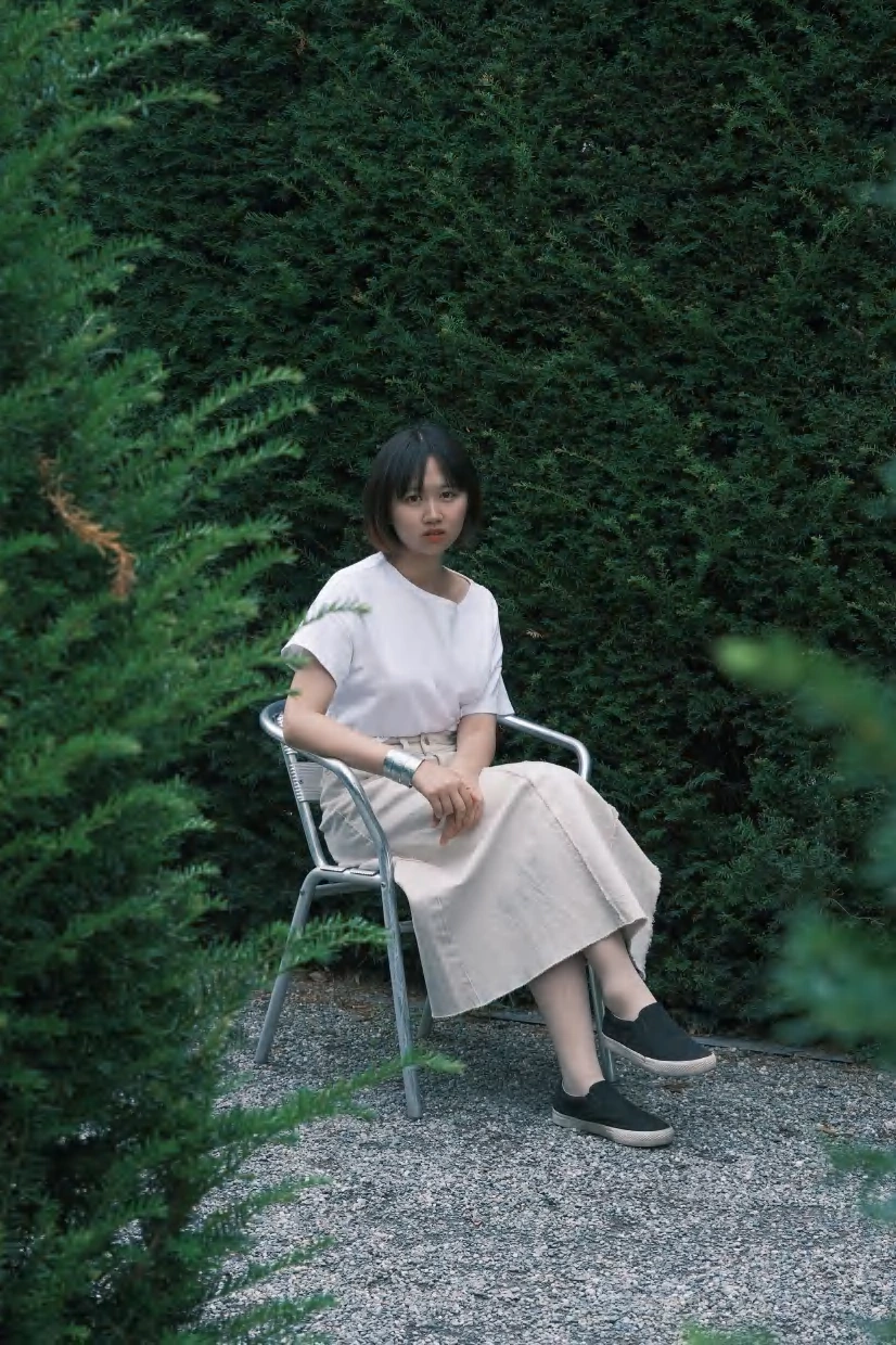 Yanzhi Yang seated beside green foliage